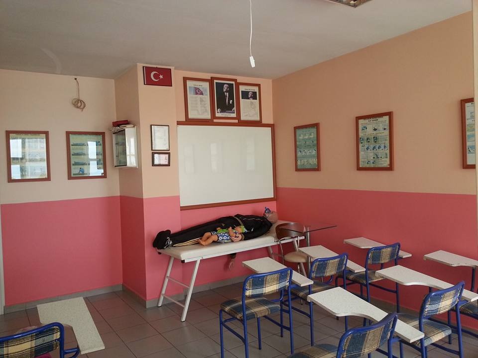 İlk yardım dersliği: beyaz tahta, uygulama mankeni, ilk yardım afişleri ve kolçaklı sıralar